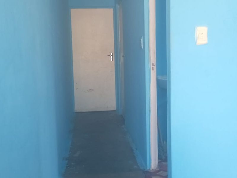 A narrow interior hallway featuring blue painted walls, a ceiling light fixture, and access to adjacent rooms.