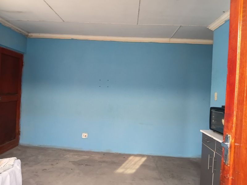 An empty living area featuring blue painted walls, coving, and basic built-in cabinetry. The space requires cosmetic updates to improve its overall condition.