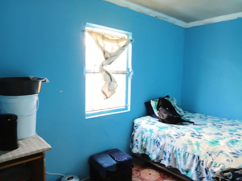 A bedroom featuring bright blue walls, tiled flooring, and a window fitted with security bars.