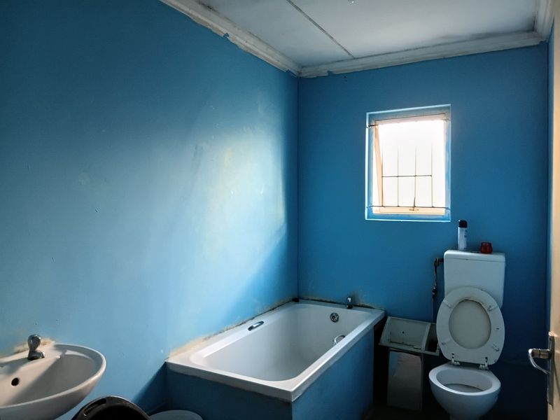 A basic bathroom featuring a built-in bathtub, pedestal basin, and toilet, requiring cosmetic updates and wall refinishing to improve its overall condition.