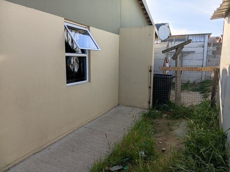 Rear exterior view of the property showing a concrete pathway, boundary wall, and window access, requiring maintenance and landscaping.