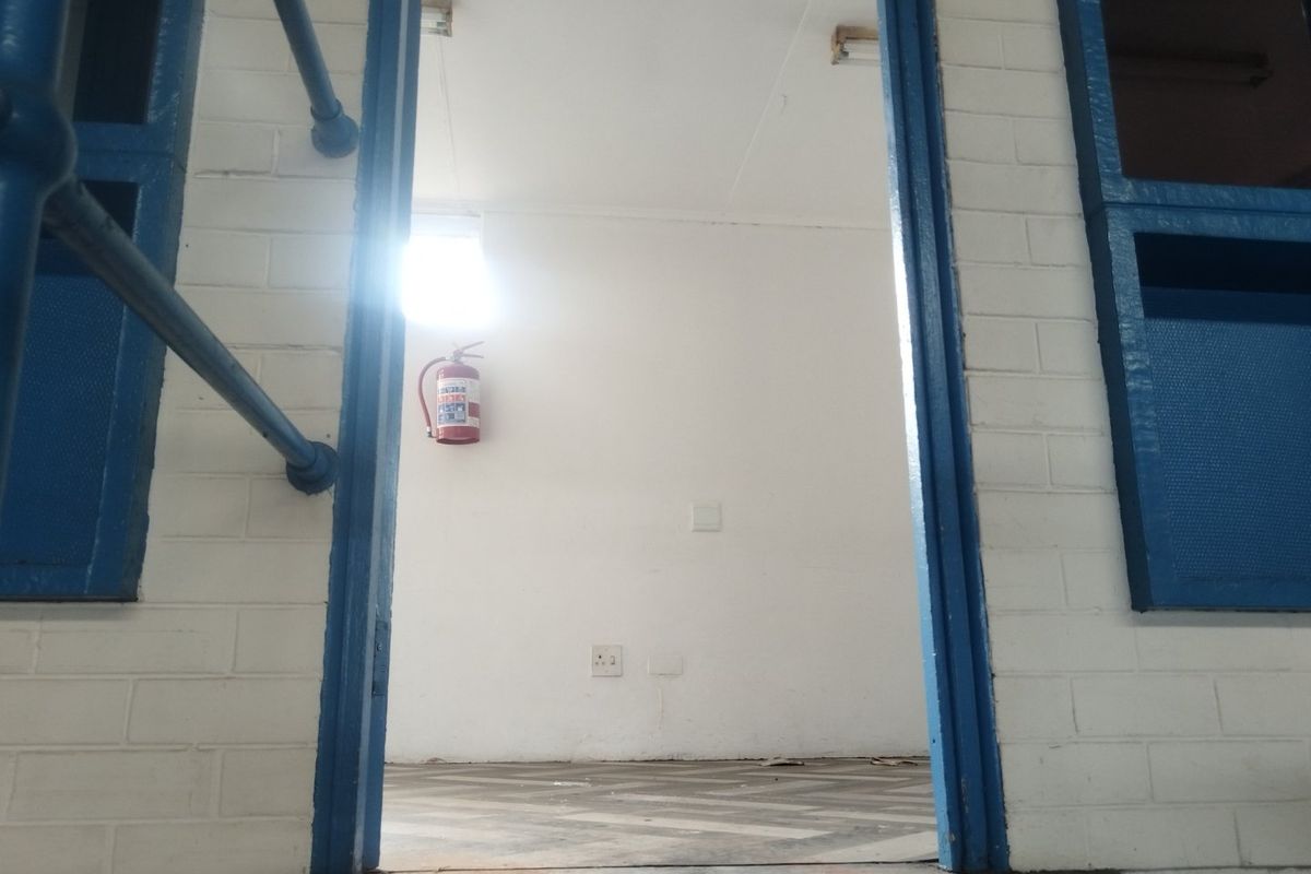 A functional utility space featuring painted brick walls, vinyl flooring, and a wall-mounted fire extinguisher, suitable for various industrial or storage purposes.