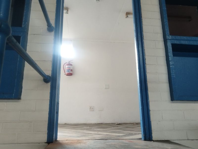 A functional utility space featuring painted brick walls, vinyl flooring, and a wall-mounted fire extinguisher, suitable for various industrial or storage purposes.