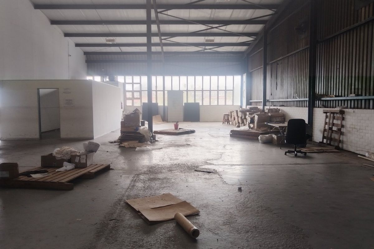 Spacious industrial warehouse unit featuring high ceilings with exposed steel trusses, concrete flooring, and large windows providing ample natural light.