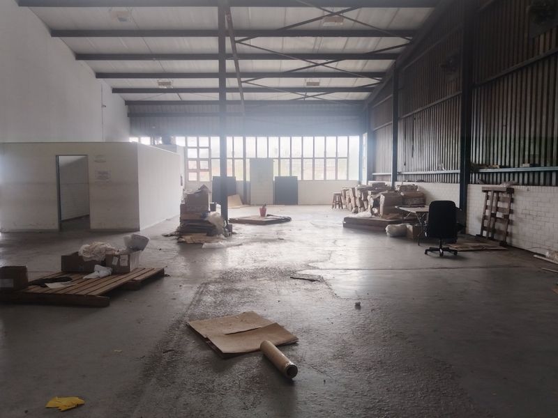 Spacious industrial warehouse unit featuring high ceilings with exposed steel trusses, concrete flooring, and large windows providing ample natural light.