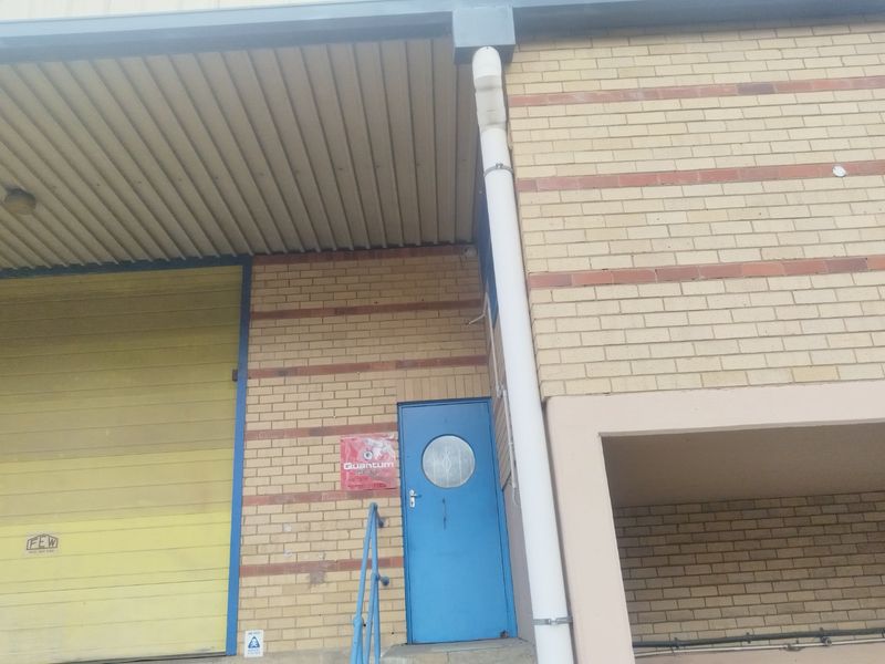 Industrial property entrance featuring a yellow roller shutter door, a blue security door, and brick facade construction.