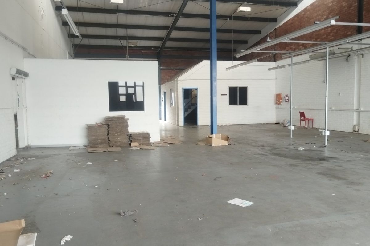 Spacious industrial warehouse unit featuring high ceilings with exposed steel trusses, concrete flooring, and partitioned office or storage areas.