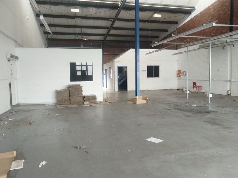 Spacious industrial warehouse unit featuring high ceilings with exposed steel trusses, concrete flooring, and partitioned office or storage areas.