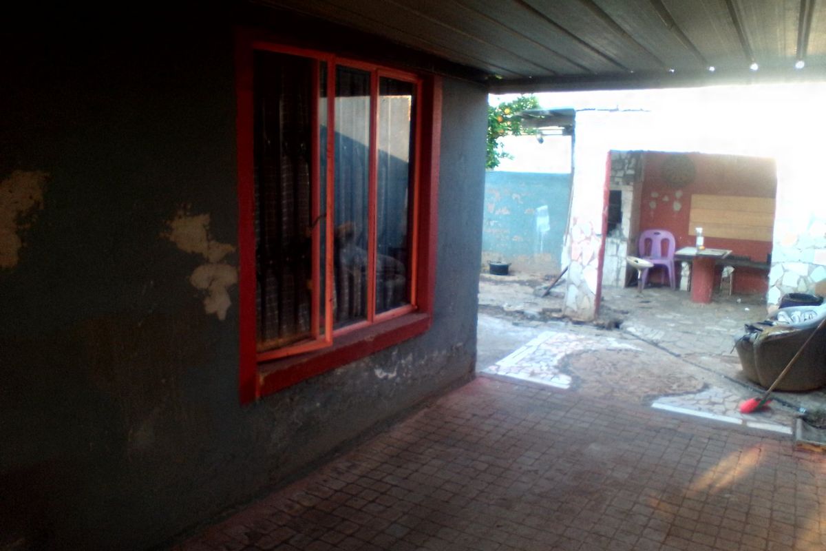 A covered outdoor patio area featuring paved flooring and a window with security bars, showing signs of wear and requiring maintenance.