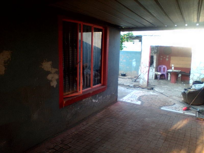 A covered outdoor patio area featuring paved flooring and a window with security bars, showing signs of wear and requiring maintenance.