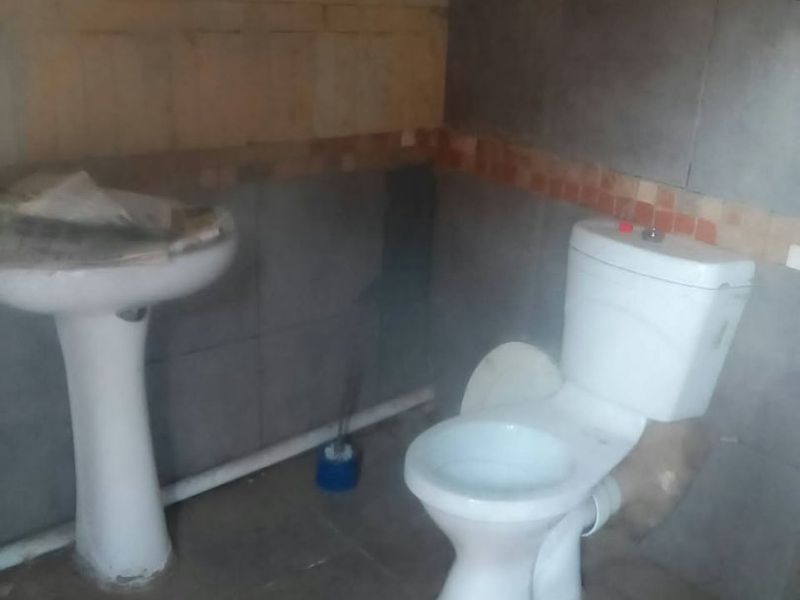 A small bathroom featuring a pedestal basin and toilet with partially tiled walls, currently in need of renovation and repair.