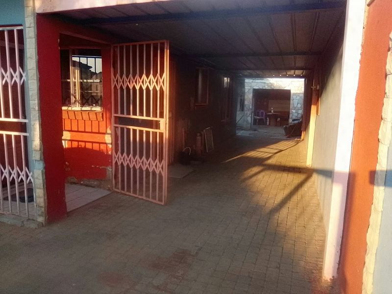 A covered carport area featuring paved flooring and metal security gates, providing secure off-street parking space.
