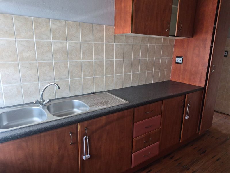 A functional kitchen area featuring laminate cabinetry, a stainless steel double sink, and tiled backsplash, currently in need of cosmetic updates.