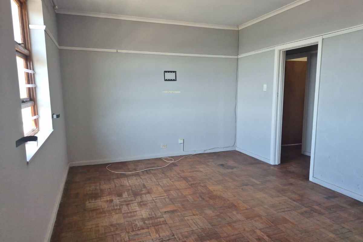 An empty living room featuring original parquet flooring, timber window frames, and classic picture rails, offering a blank canvas for renovation.