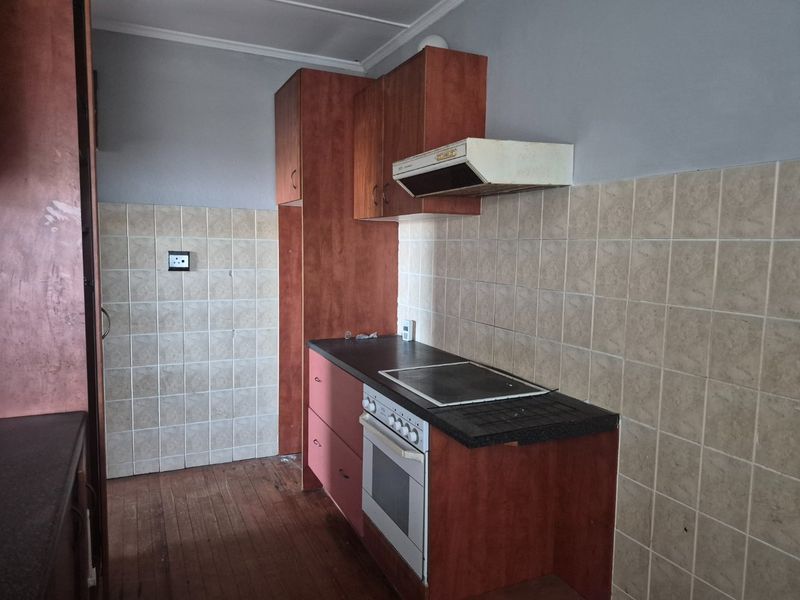 A dated kitchen featuring wooden cabinetry, a built-in oven with hob, extractor fan, and tiled backsplash, offering potential for a modern renovation.