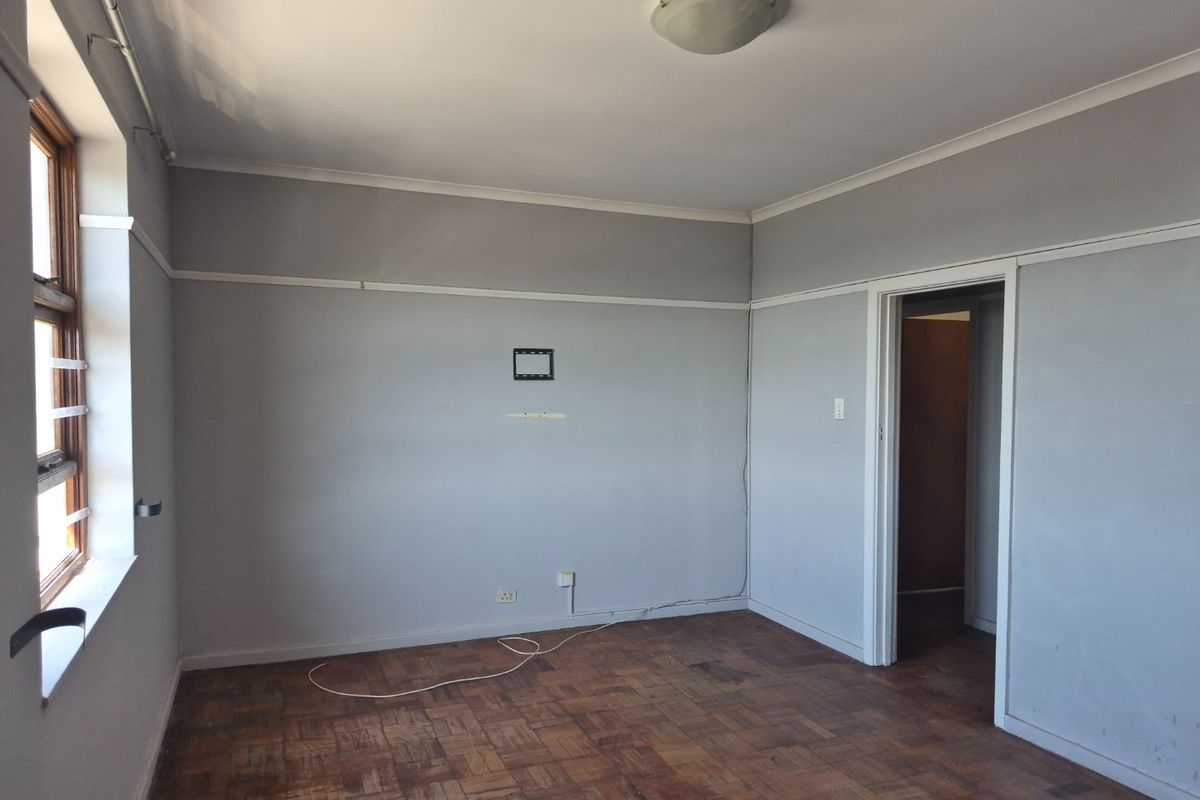 An empty bedroom featuring original parquet flooring, neutral grey walls with picture rails, and a timber-framed window with security bars.