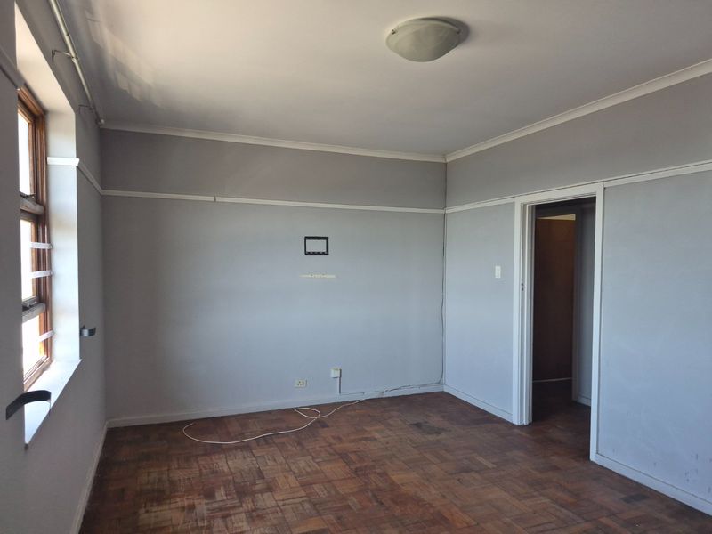 An empty bedroom featuring original parquet flooring, neutral grey walls with picture rails, and a timber-framed window with security bars.