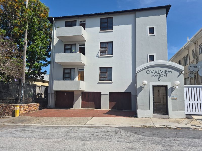 Front elevation of Ovalview Mansions, featuring a multi-story apartment block with balconies, ground-level garage access, and a secure pedestrian entrance.
