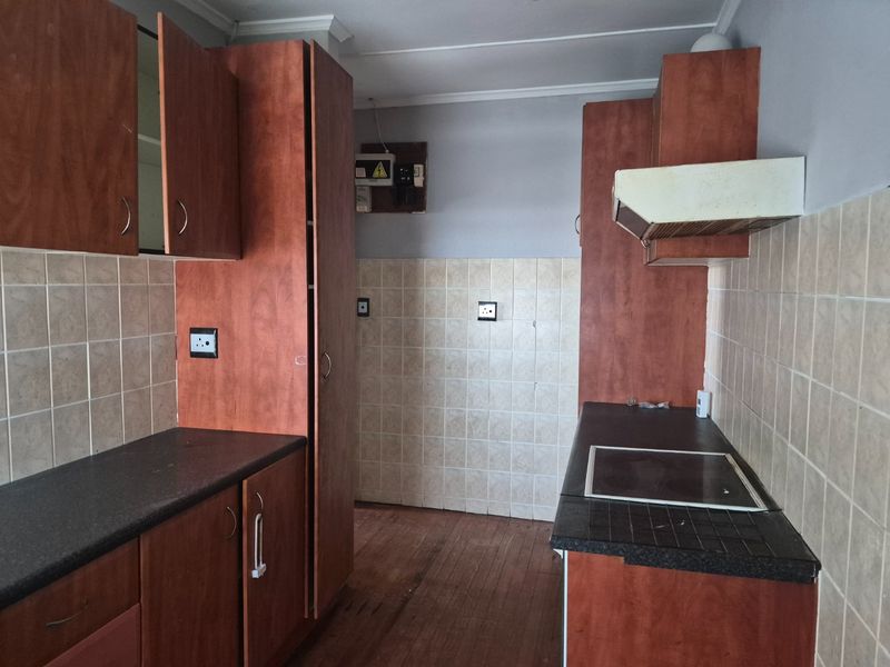 A dated kitchen featuring laminate cabinetry, tiled splashbacks, and a built-in electric hob with an extractor fan.