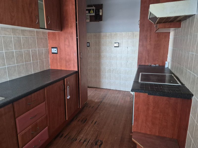 A dated kitchen featuring timber cabinetry, laminate countertops, tiled backsplash, and an electric hob, requiring cosmetic updates to modernize the space.