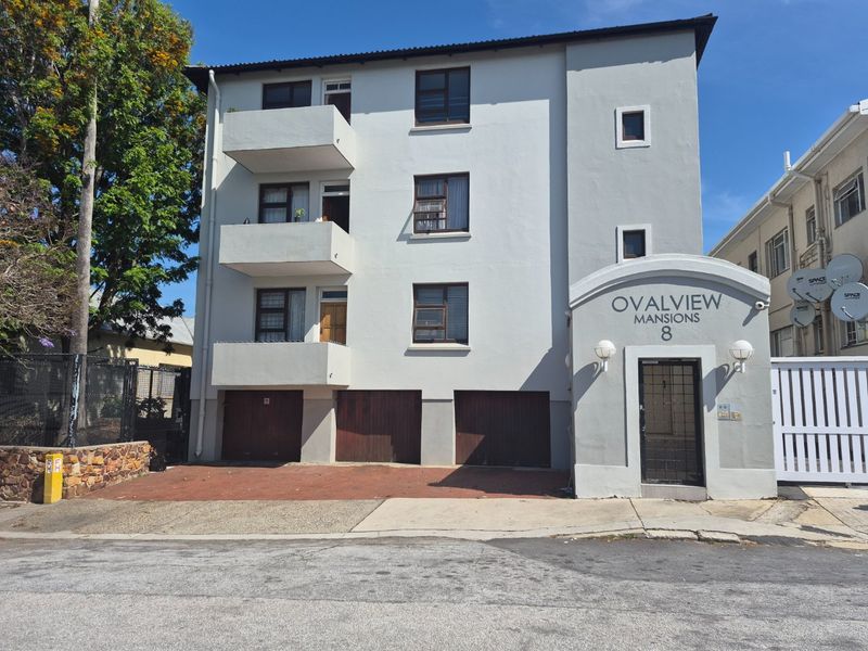 Front elevation of Ovalview Mansions, featuring a multi-story apartment block with balconies, ground-level garage access, and a secure pedestrian entrance.