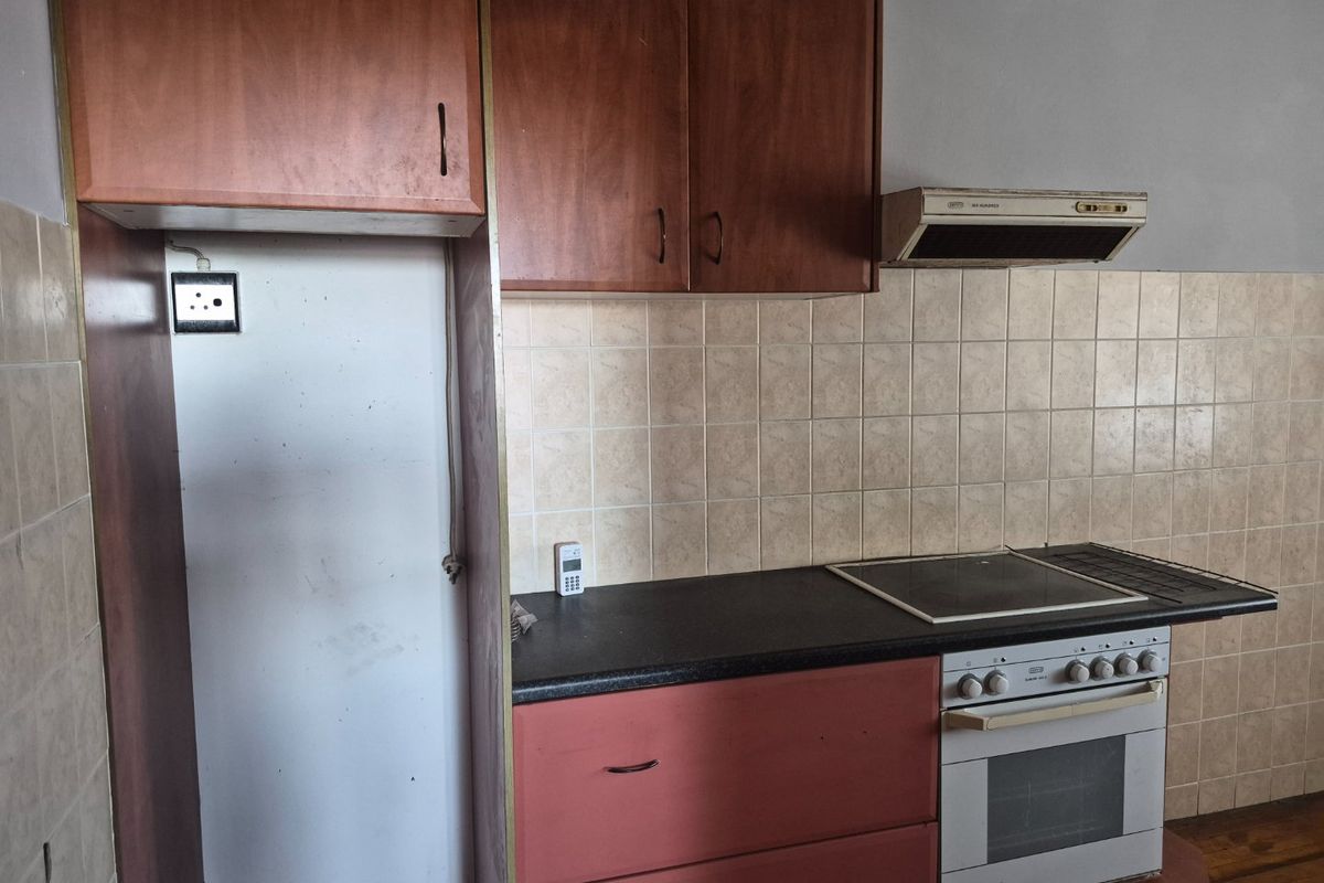A functional kitchen featuring built-in cabinetry, an electric oven with hob, extractor fan, and tiled backsplash, offering a blank canvas for renovation.