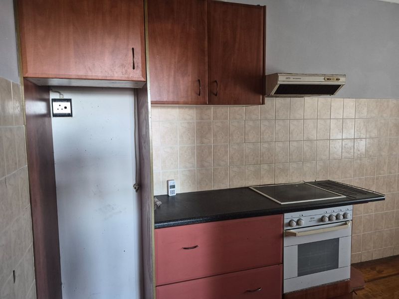 A functional kitchen featuring built-in cabinetry, an electric oven with hob, extractor fan, and tiled backsplash, offering a blank canvas for renovation.