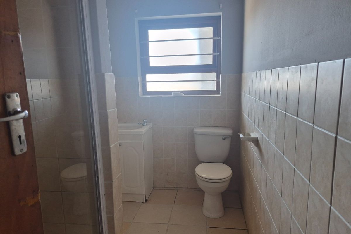 A functional bathroom featuring a toilet, vanity basin, and shower enclosure with neutral ceramic tiling throughout.