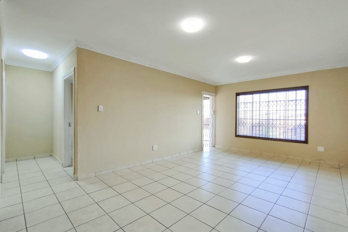 A spacious, empty living area featuring neutral tiled flooring, coved cornicing, and secure window bars, offering a blank canvas for interior design.