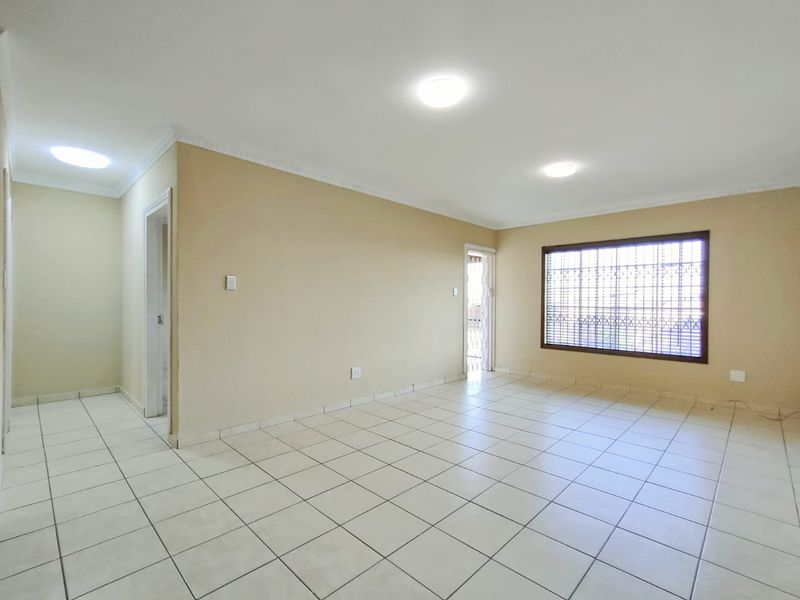 A spacious, empty living area featuring neutral tiled flooring, coved cornicing, and secure window bars, offering a blank canvas for interior design.