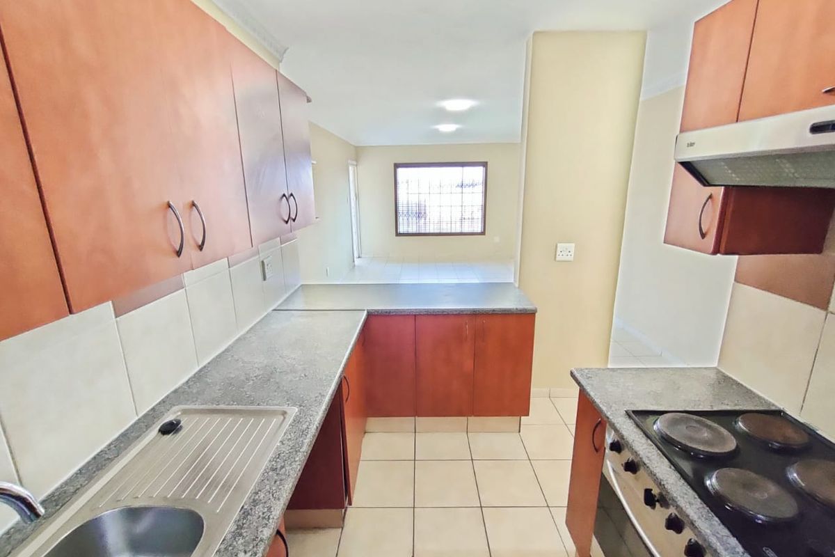 A functional kitchen featuring built-in cabinetry, laminate countertops, a stainless steel sink, and integrated electric cooking appliances, leading into an open-plan living area.