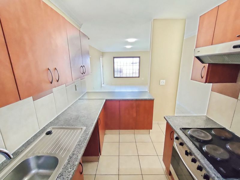 A functional kitchen featuring built-in cabinetry, laminate countertops, a stainless steel sink, and integrated electric cooking appliances, leading into an open-plan living area.