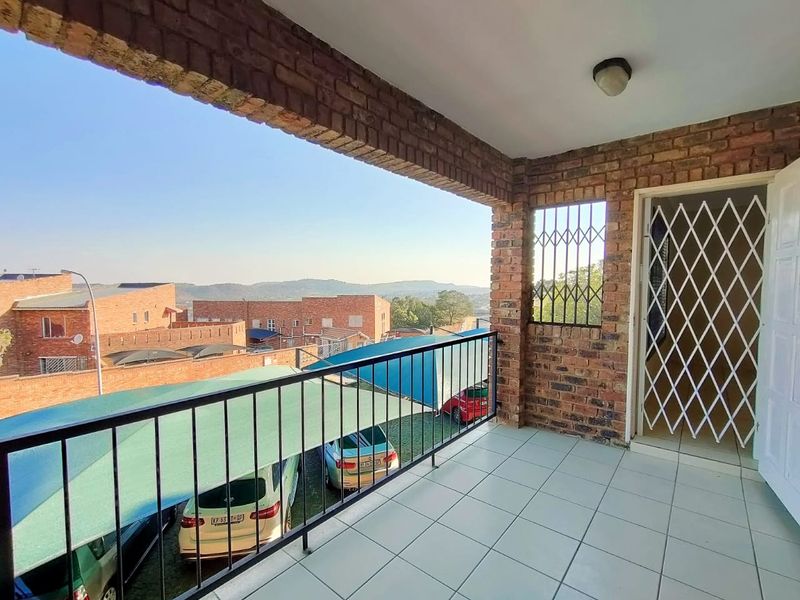 A covered balcony featuring brick masonry walls, tiled flooring, and metal security fixtures, offering an elevated view of the surrounding complex and landscape.
