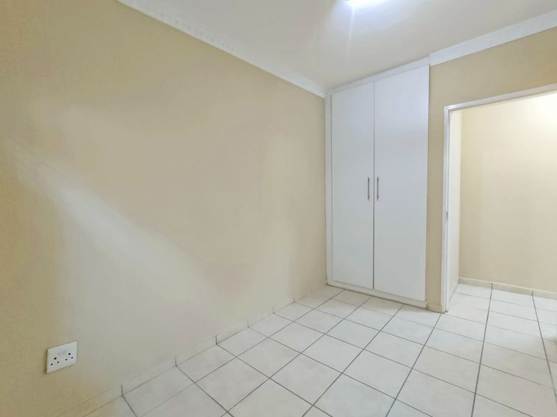 A clean, empty bedroom featuring white tiled flooring, neutral walls, and a built-in white wardrobe with modern handles.