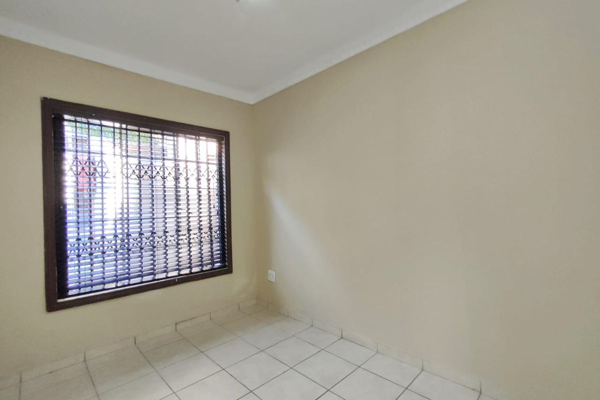 A clean, empty bedroom featuring neutral tiled flooring, coving, and a window fitted with security burglar bars.