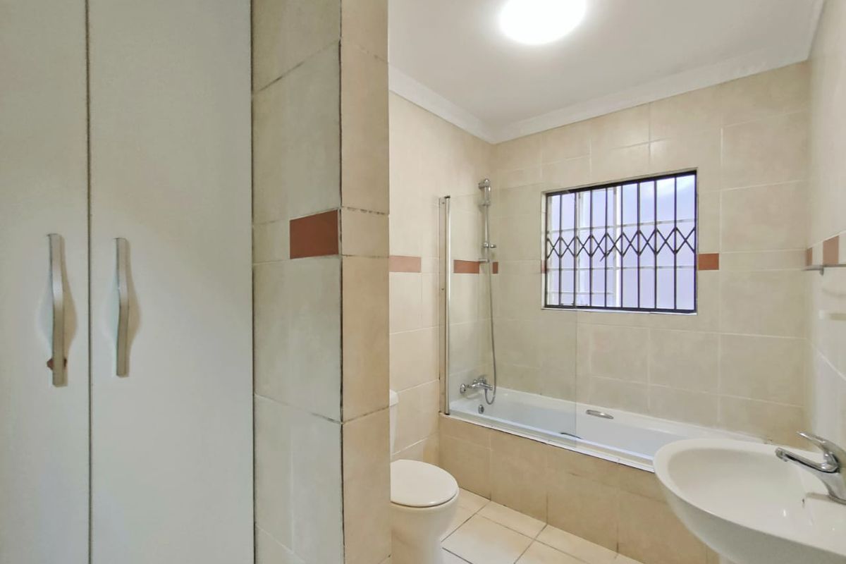 A functional bathroom featuring a bathtub with a glass shower screen, a pedestal basin, a toilet, and built-in storage cabinetry.