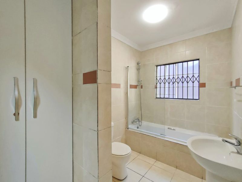 A functional bathroom featuring a bathtub with a glass shower screen, a pedestal basin, a toilet, and built-in storage cabinetry.
