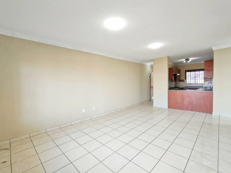 An open-plan living and kitchen area featuring tiled flooring, neutral walls, and functional kitchen cabinetry with laminate countertops.