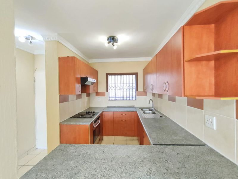 A functional kitchen featuring wooden cabinetry, laminate countertops, a built-in oven with gas hob, and a tiled backsplash.