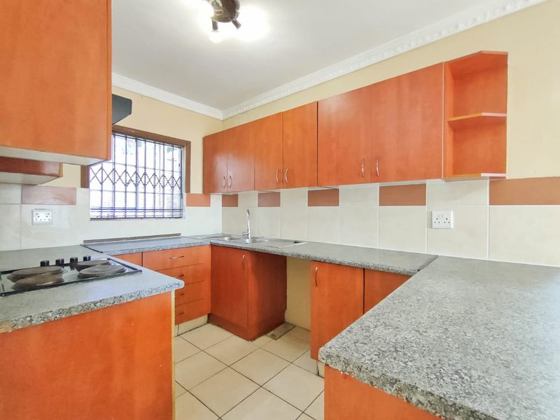 A functional kitchen featuring orange laminate cabinetry, granite countertops, a built-in hob, and tiled backsplash, offering a clean and practical workspace.