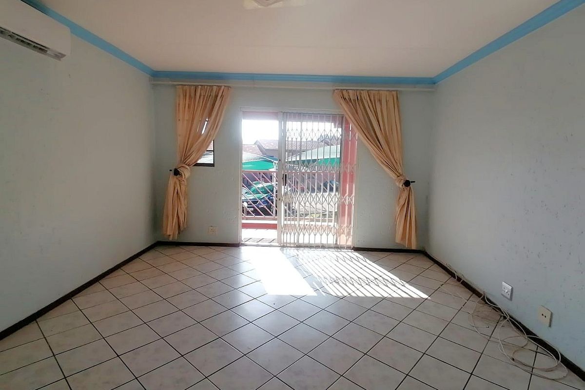 An empty living room featuring tiled flooring, a split-system air conditioner, and a sliding glass door with a security gate leading to the exterior.