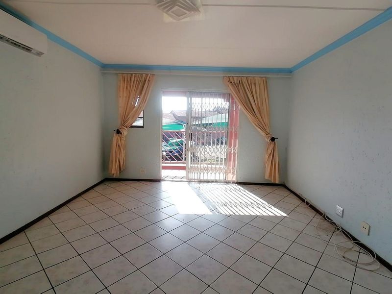 An empty living room featuring tiled flooring, a split-system air conditioner, and a sliding glass door with a security gate leading to the exterior.