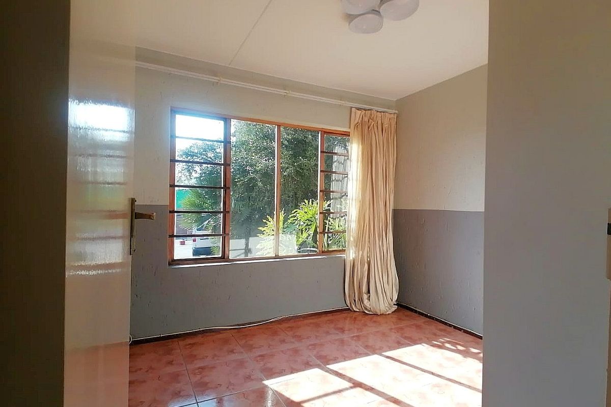 An empty bedroom featuring tiled flooring and a large window, providing a blank canvas for potential renovation and interior design updates.