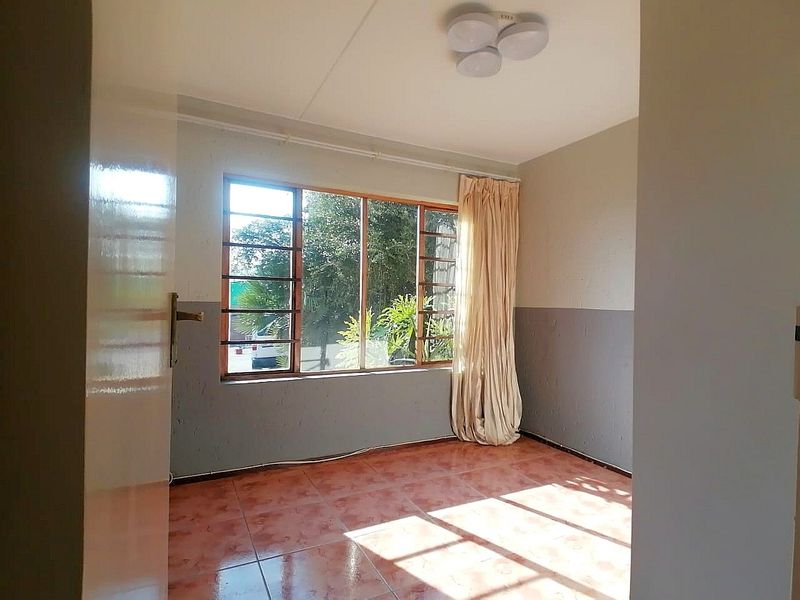 An empty bedroom featuring tiled flooring and a large window, providing a blank canvas for potential renovation and interior design updates.