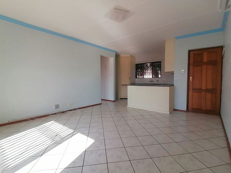 An open-plan living and kitchen area featuring tiled flooring, built-in cabinetry, and a timber entrance door, offering a blank canvas for renovation.
