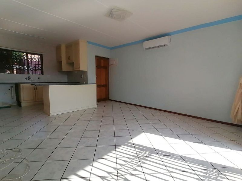 Open-plan living and kitchen area featuring tiled flooring, built-in cabinetry, and a wall-mounted air conditioning unit.