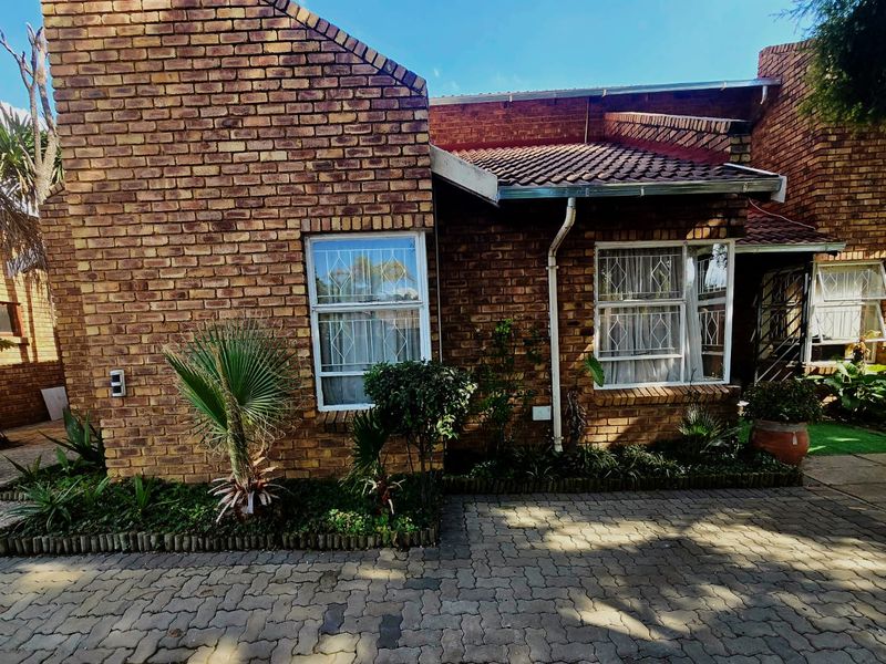 Front elevation of a face-brick house featuring a tiled roof, security-barred windows, and a paved driveway entrance.