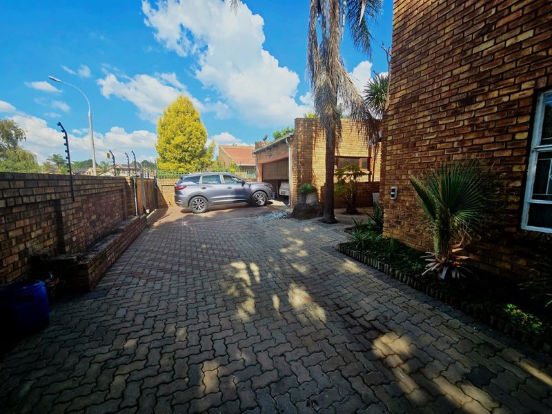 Front exterior view of the property featuring a paved driveway, face brick facade, and secure perimeter wall with electric fencing.