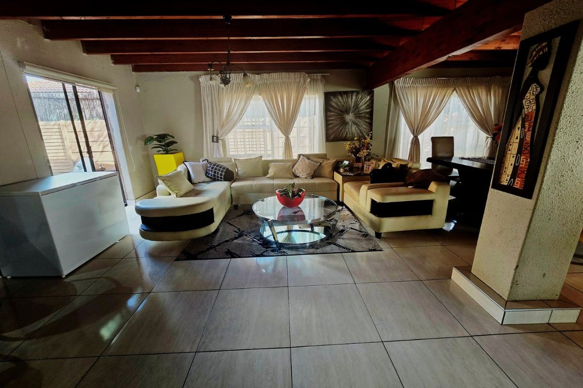 Spacious living area featuring exposed timber ceiling beams, large format floor tiles, and a sliding glass door providing access to the exterior.