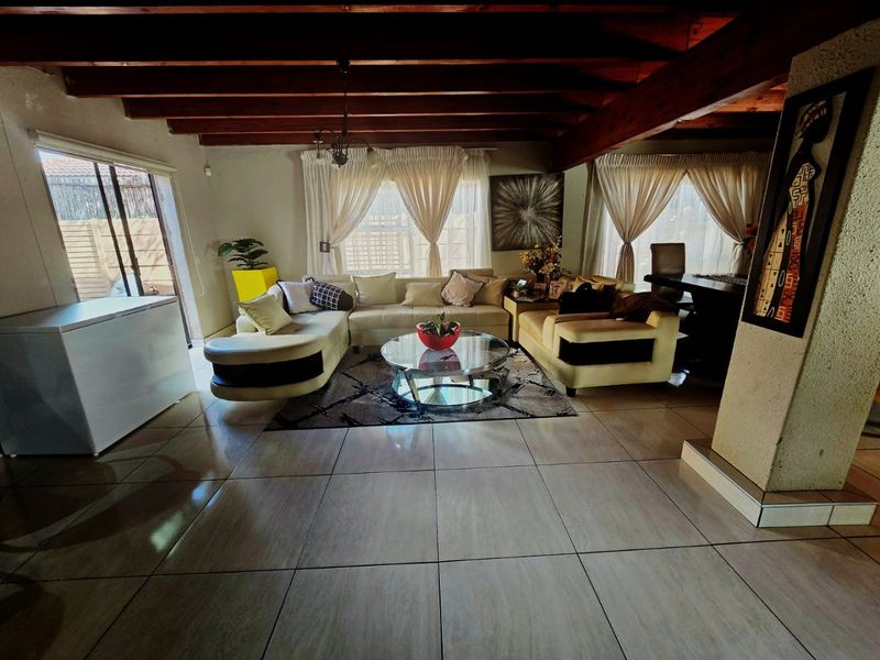 Spacious living area featuring exposed timber ceiling beams, large format floor tiles, and a sliding glass door providing access to the exterior.